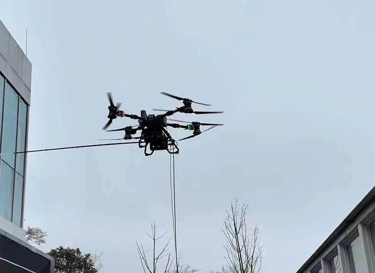 DJI FC100 tethered drone cleaning a glass facade with a ground-fed water hose.